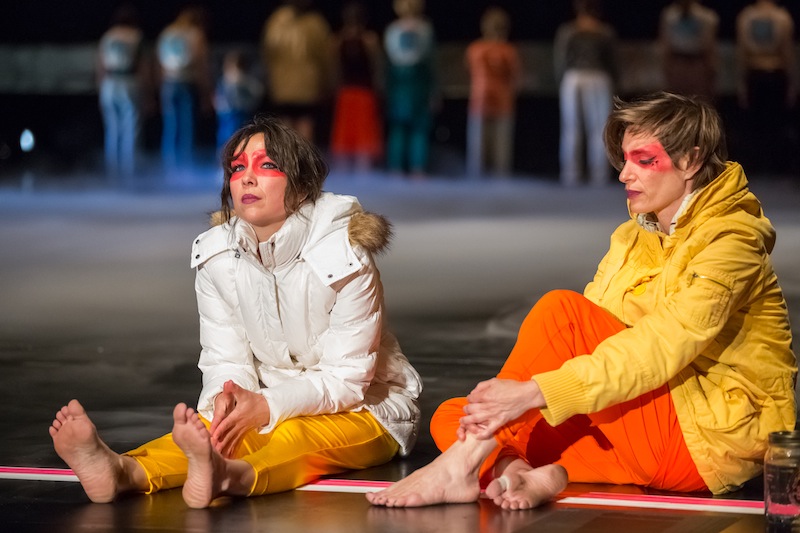 Emily Johnson and Krista Langberg sit onstage in brightly colored parks with red warrior paint on their faces
